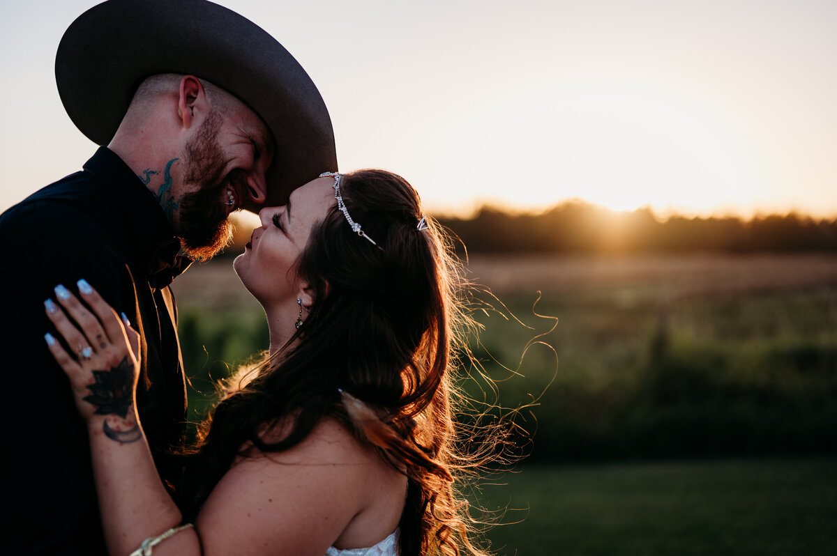 bride and groom leaning in to kiss, standing in front of a field during golden hour, with beautiful golden sun shinning on them in the background taken at The Rustic Wedding Barn in Edmonton, Alberta.