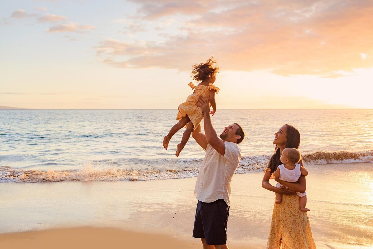 Young family lifts daughter in the air during their beach photography session with Love + Water