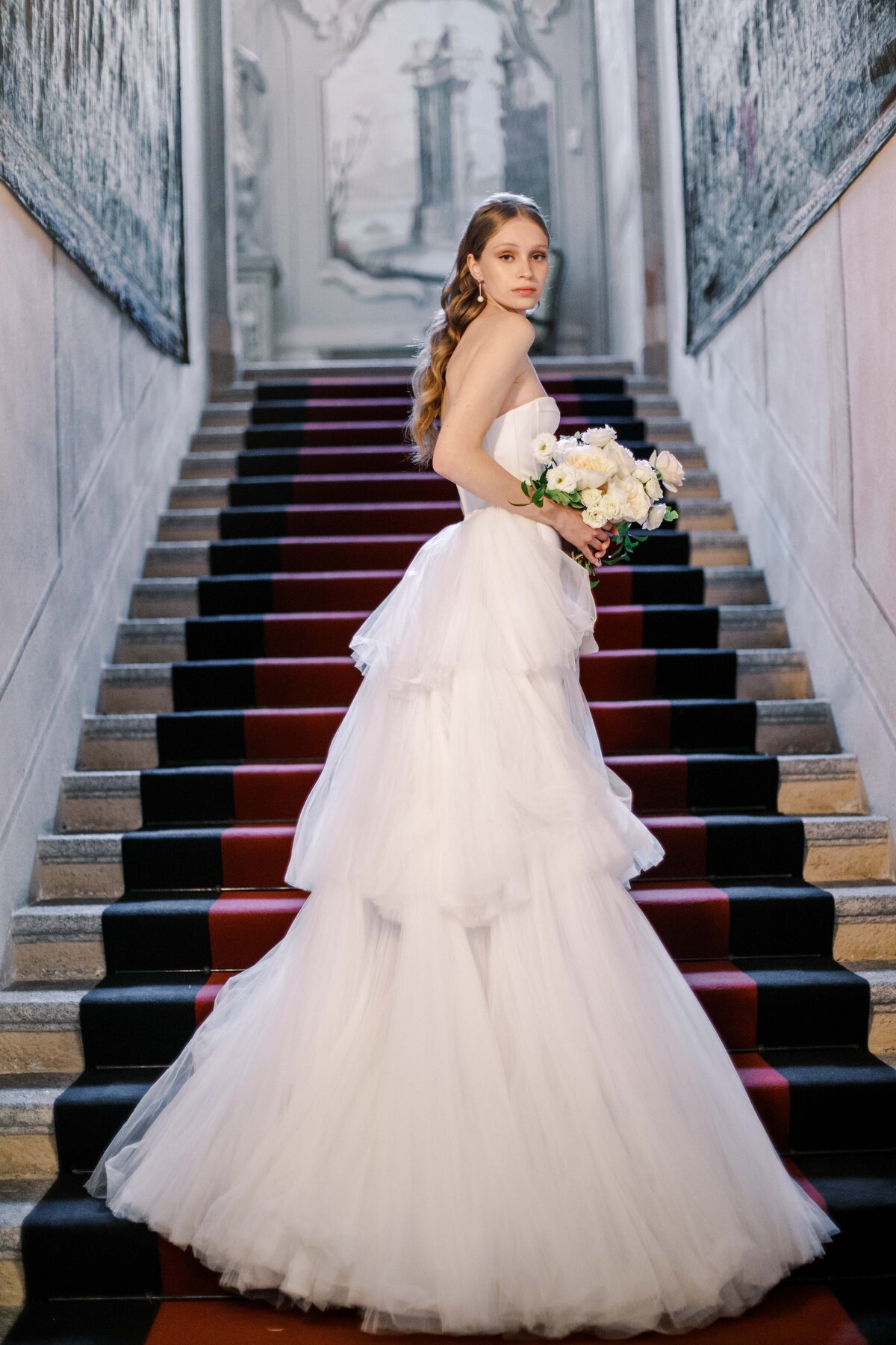 Film photograph of bride in multi tiered  strapless wedding gown standing with bouquet on the steps inside Villa Sola Cabiati for her Lake Como wedding photographed by Italy wedding photographer