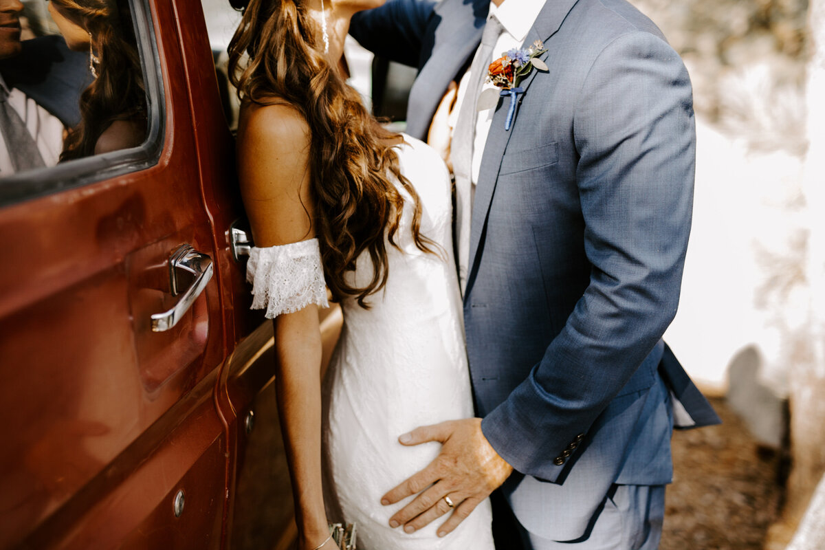 Couple leans againist a red van in wedding dress and suit