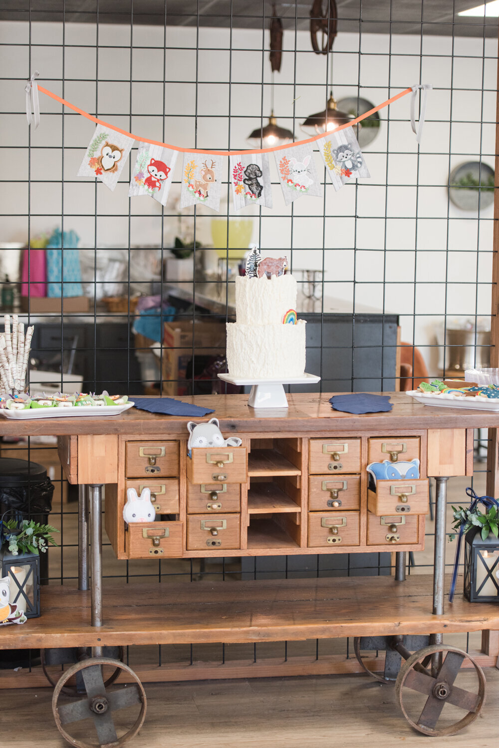 A woodland baby boy shower dessert table, displayed on a rustic wooden cart, features an assortment of sweet treats. Woodland animals peek out from the open drawers, adding a playful touch to the woodland-themed celebration in Billings, MT.