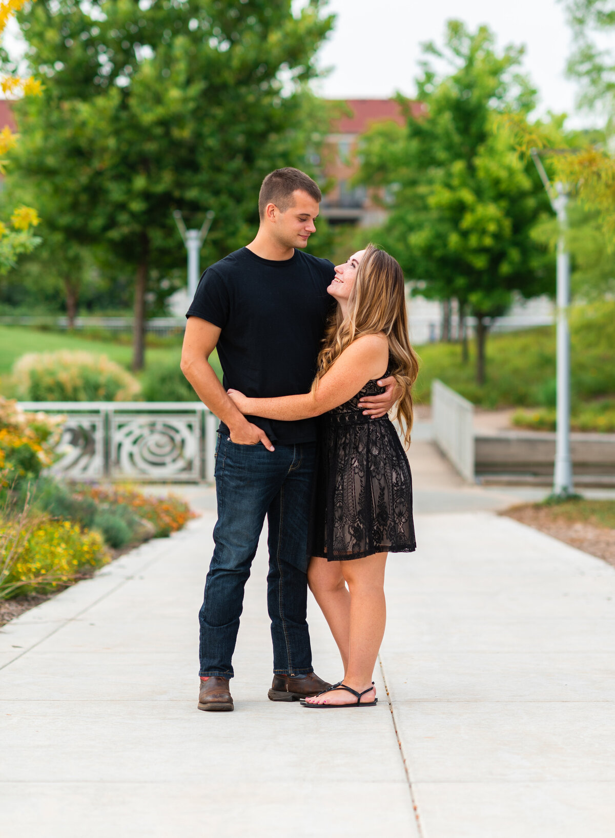 A couple standing close together, looking at each other, on a tree-lined path