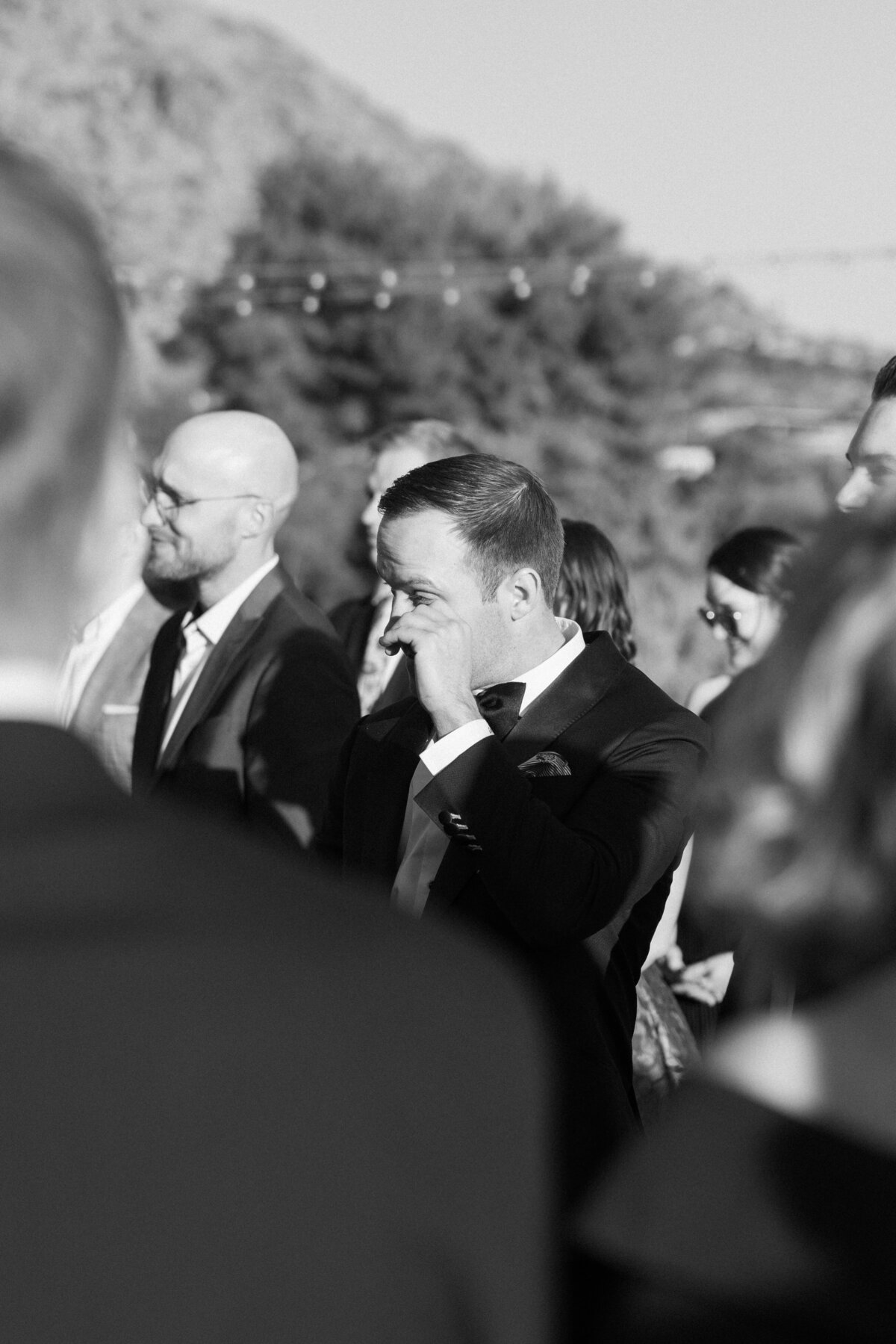 Groom wiping tear seeing bride walking down aisle at wedding ceremony
