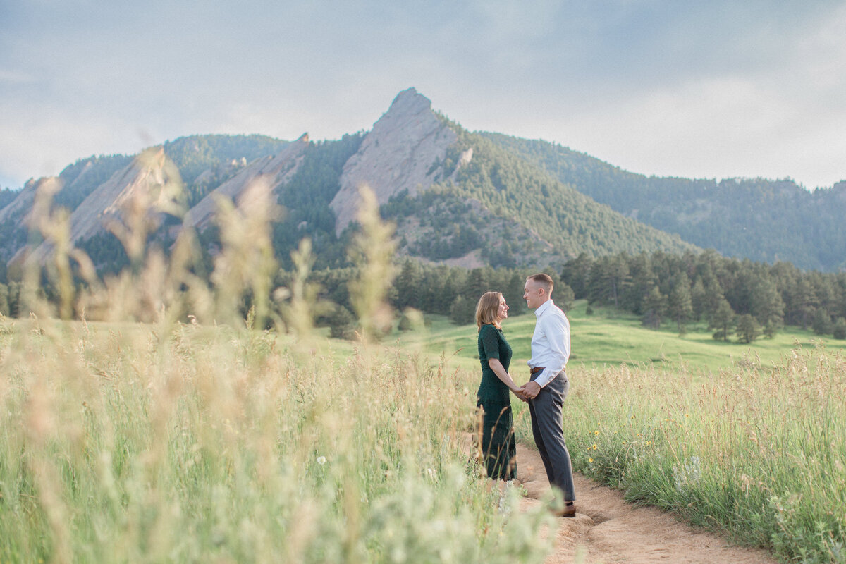 A man and woman stand looking at each other and holding hands in a meadow in the Colorado foothills