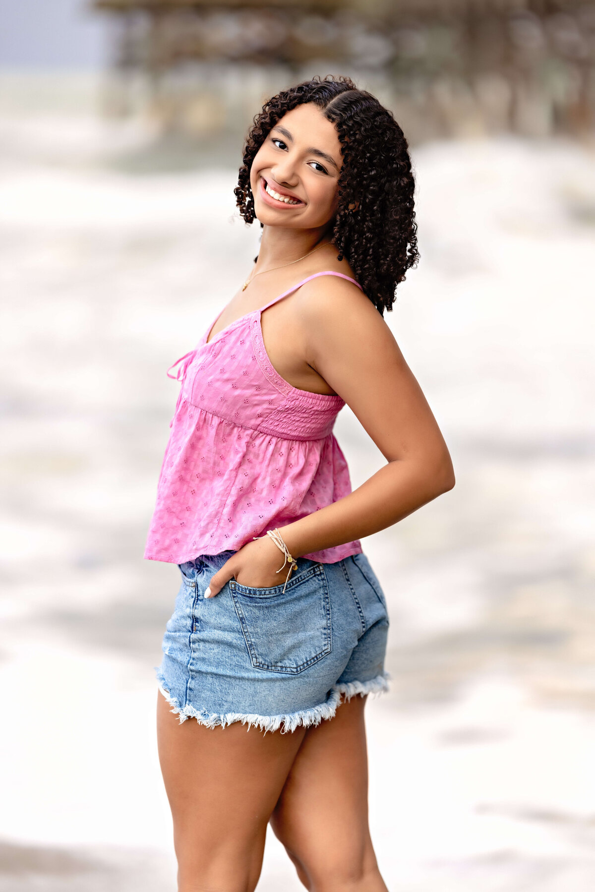 Close-up senior portrait with a girl in pink and denim looking over her shoulder, smiling playfully-modern Gen z energy at the beach.