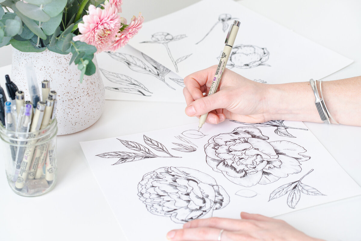 Education page for Skye McNeill Studio's online education offerings. Image shows Skye McNeill's hands drawing a detailed botanical illustration of peony flowers and birds at a desk with a jar of pens and a vase of flowers.