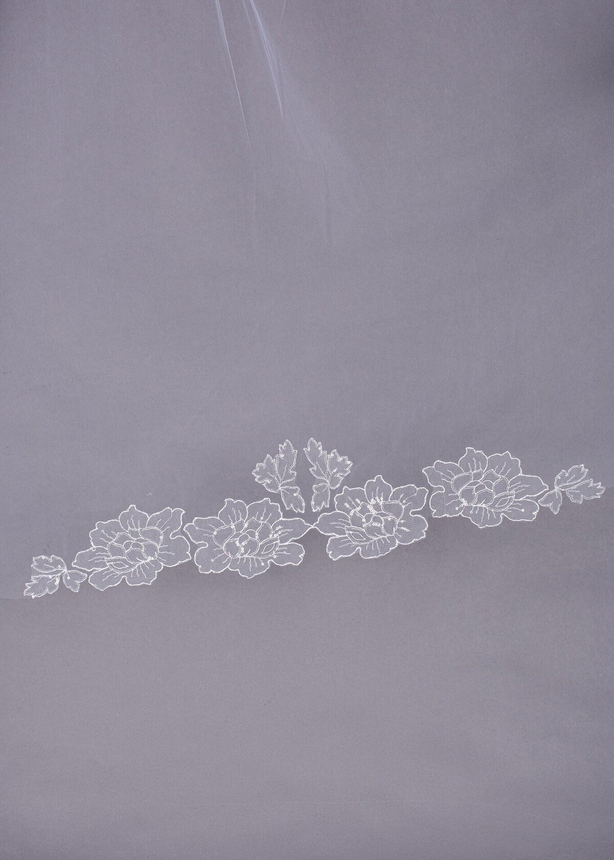 The flower appliques at the hem of the cathedral-length Orchids Veil are hand cut and hand sewn. They are accented with clear sequins for a subtle sparkle.