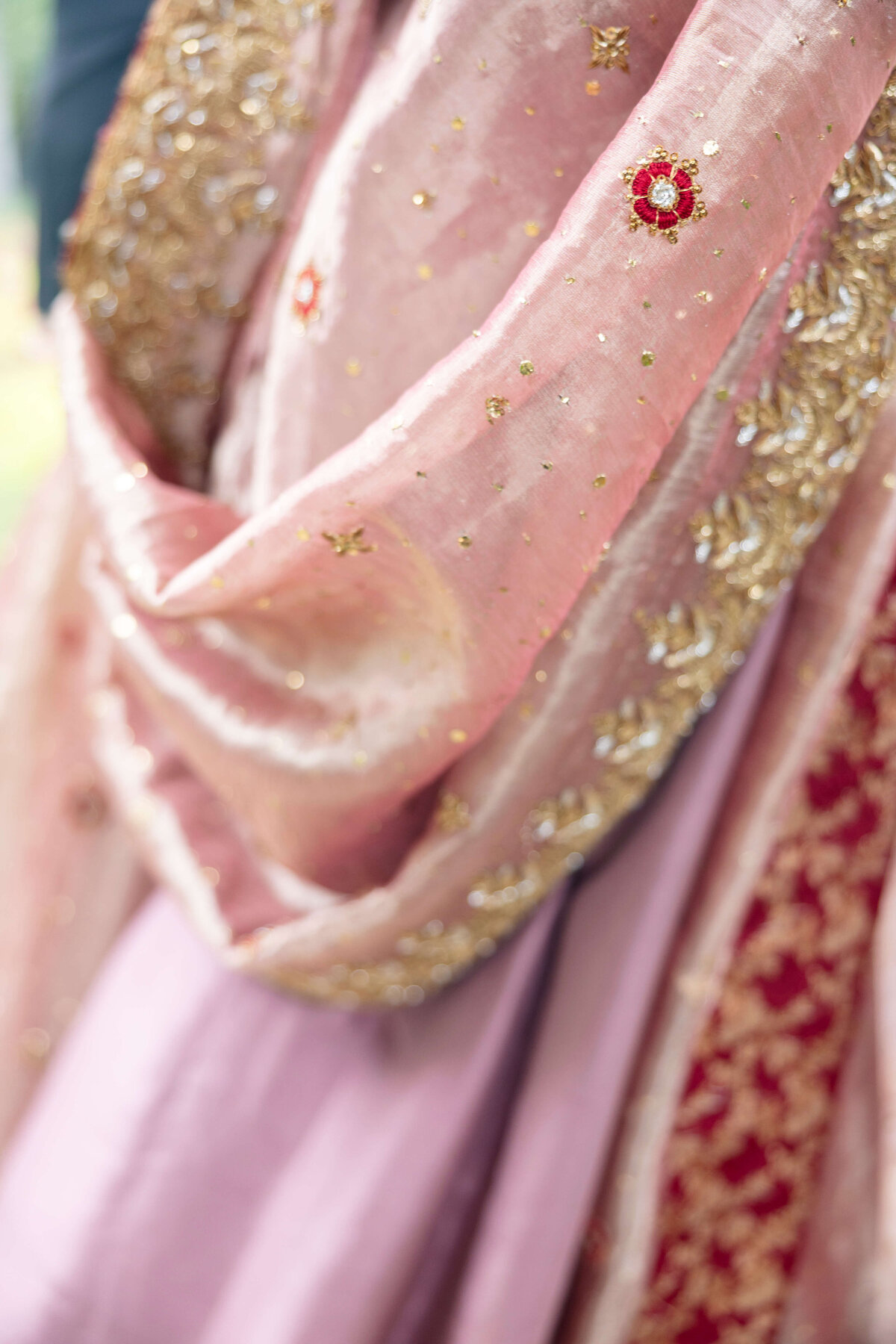Close-up of an elegant, intricately embroidered dupatta in shades of pink and gold, featuring detailed floral and geometric patterns with sparkling embellishments. The fabric drapes gracefully, showcasing its texture.