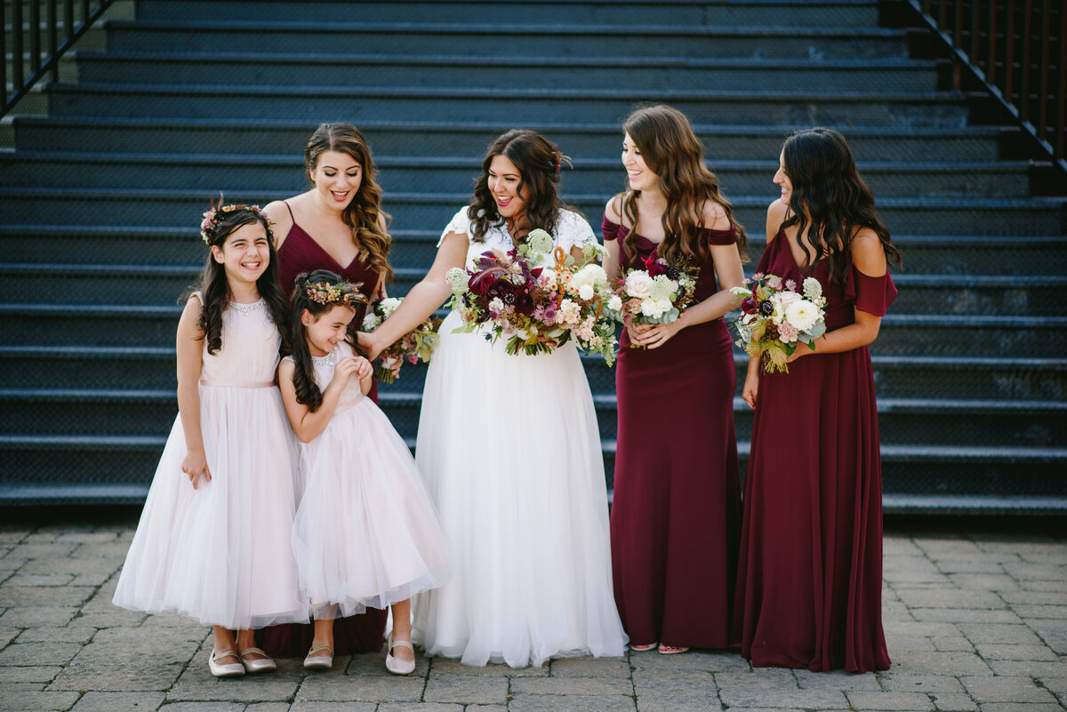 A bridal party poses by a blue staircase in Old Montreal, with two young bridesmaids laughing.