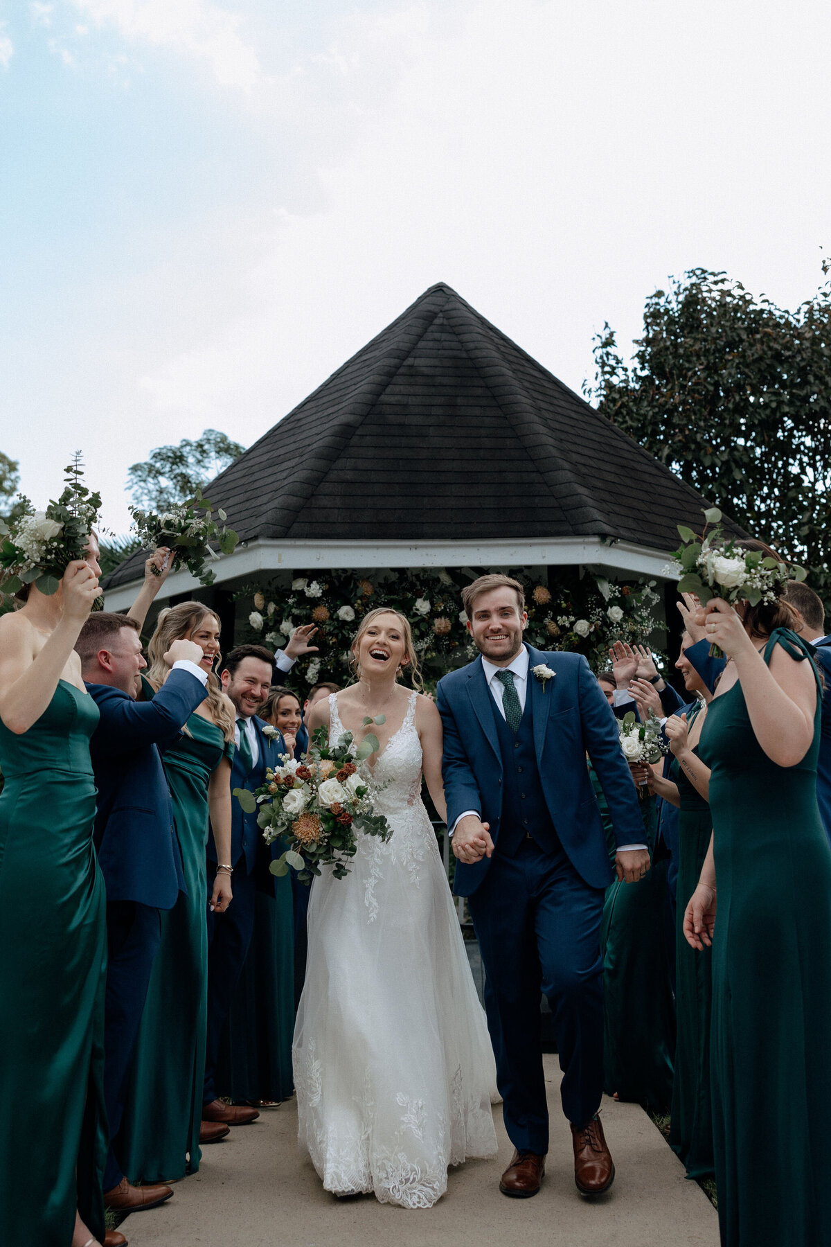 A bride and groom run through a tunnel created by their bridesmaids and groomsmen as they cheer them on.
