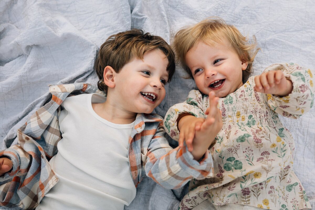 Two young siblings lying on a rug holding hands, Melbourne family photographer Delanie