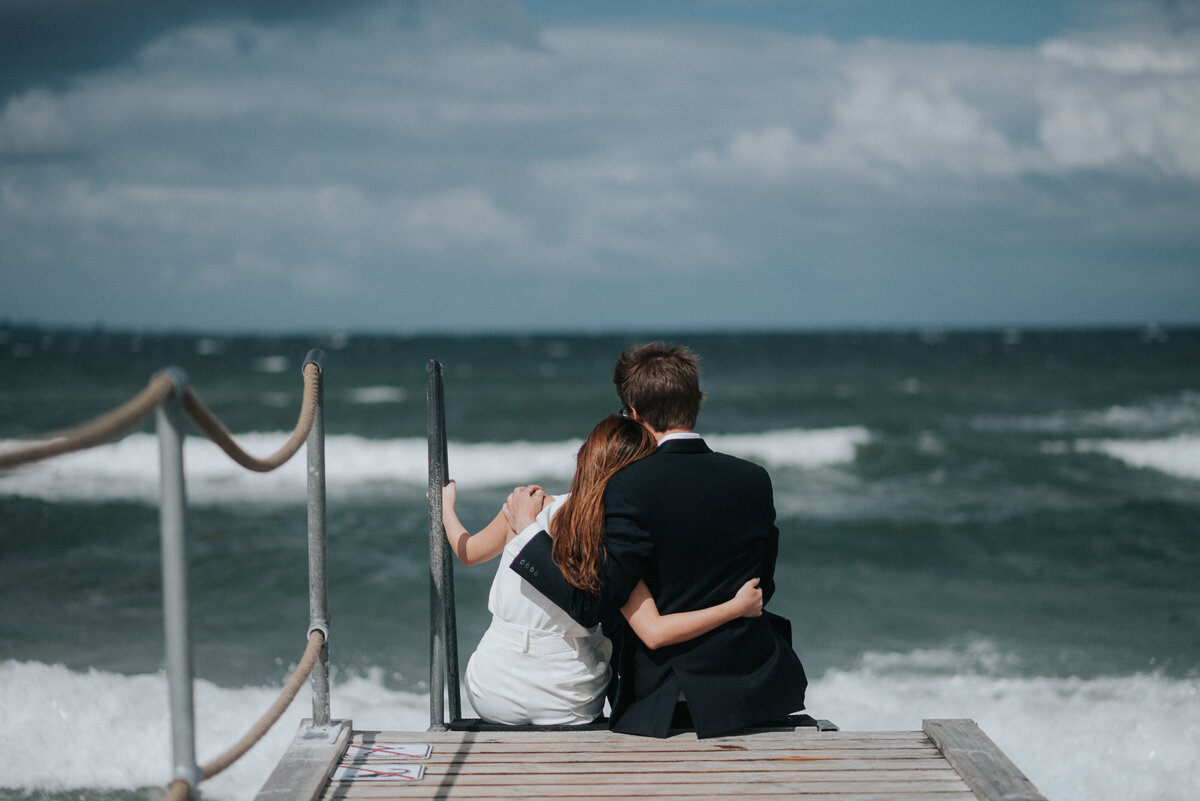 Bride and groom sitting by ocean