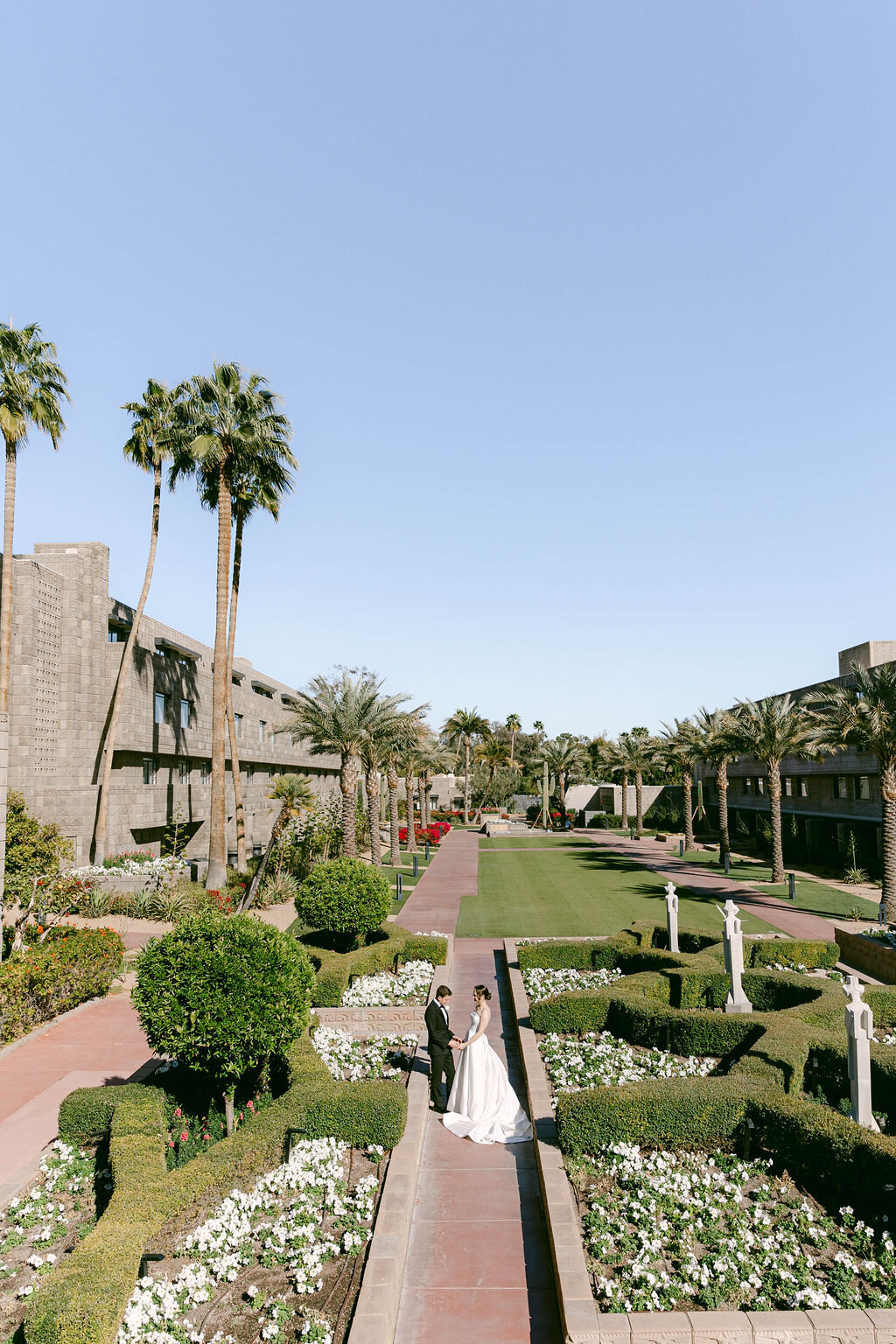 Wide view of Arizona Biltmore wedding couple standing among lush palms and flowers
