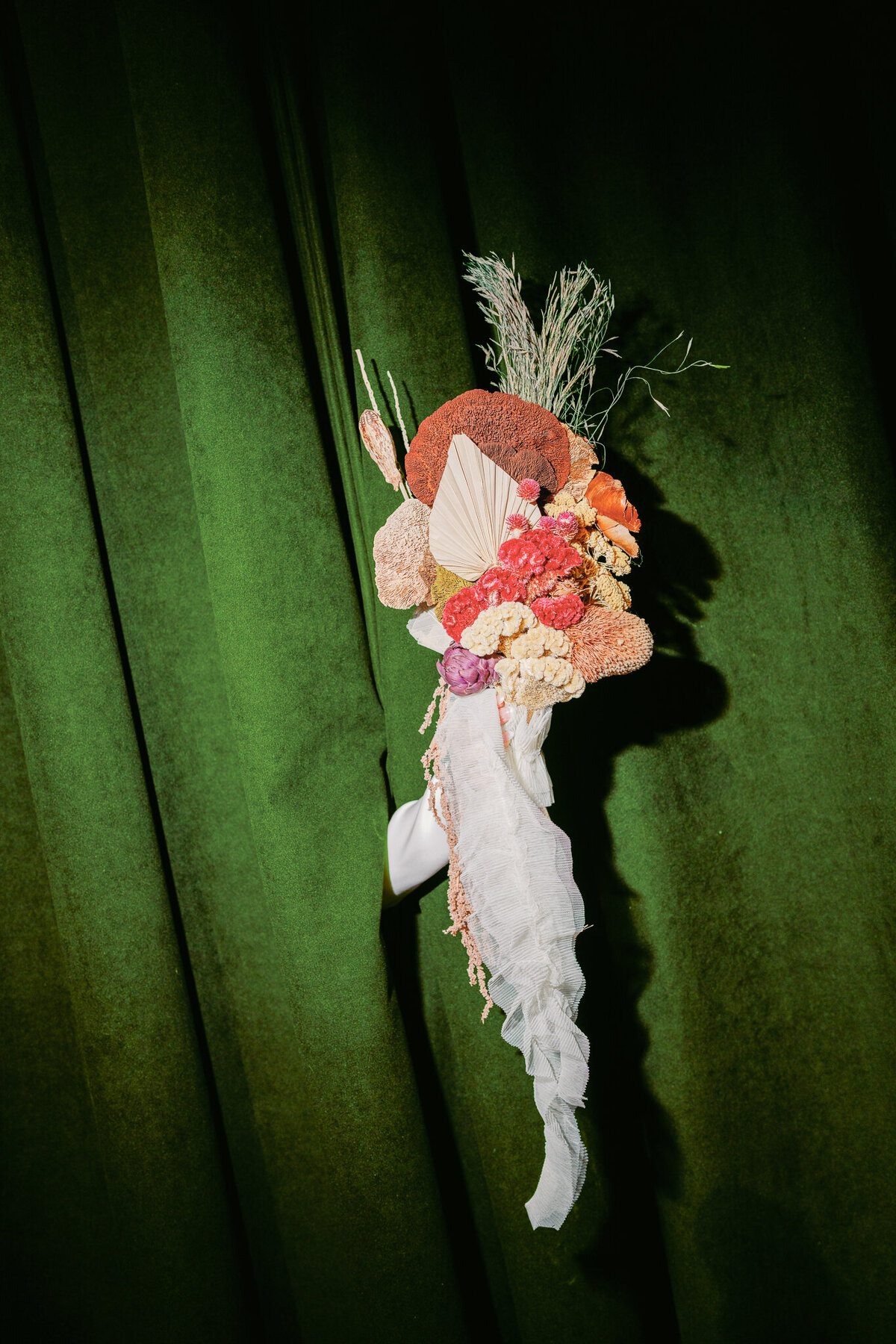 Colorful asymmetrical bridal bouquet against emerald green velvet curtain