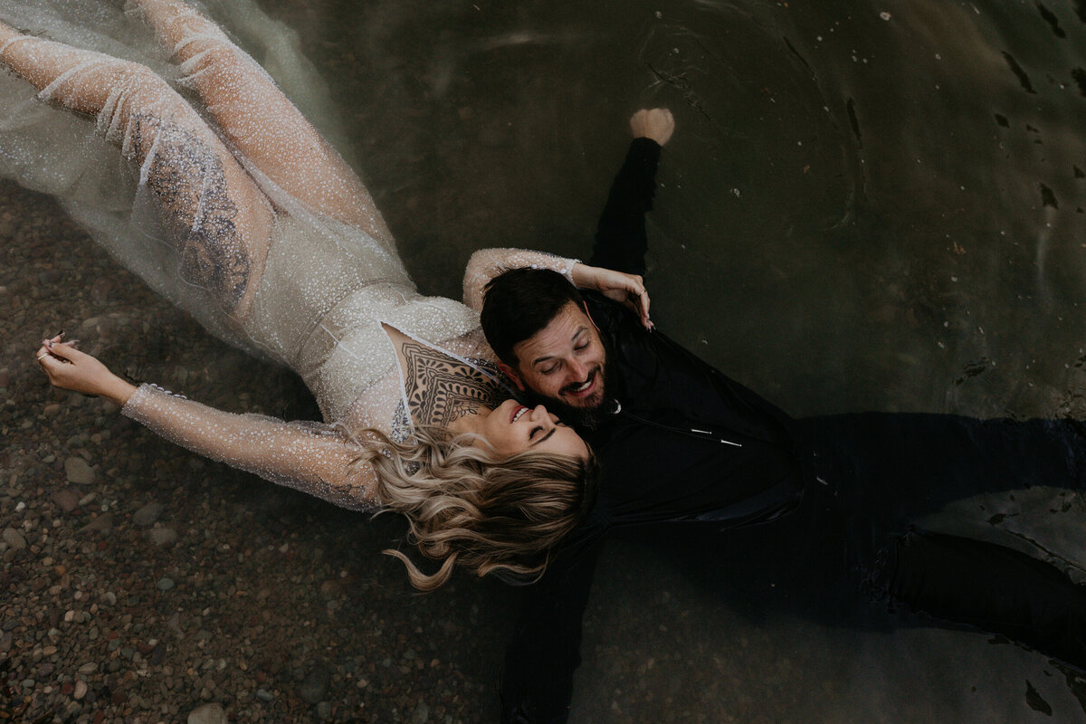 bride and groom laying together in a pond in their wedding attire