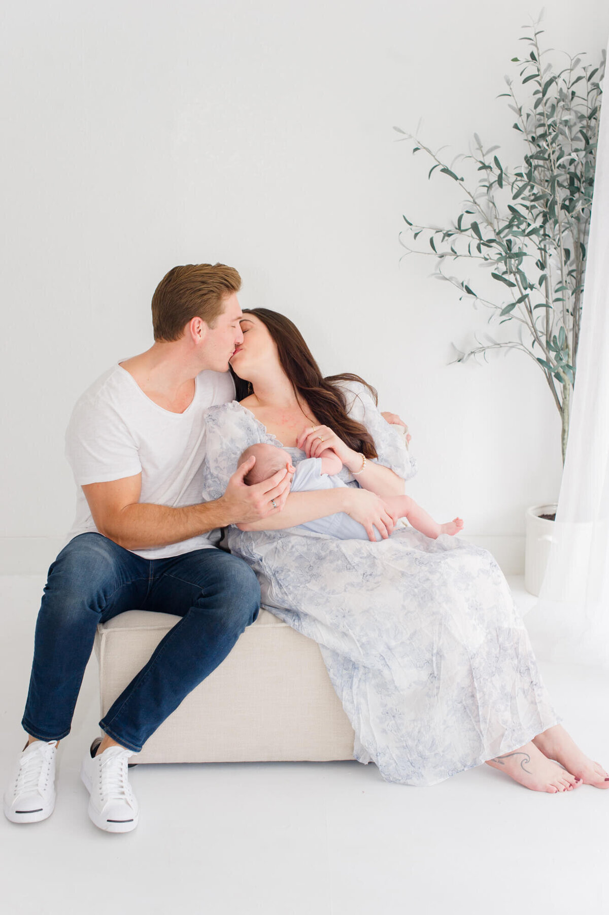 Studio image of parents kissing while holding their newborn baby in a studio in north Orlando