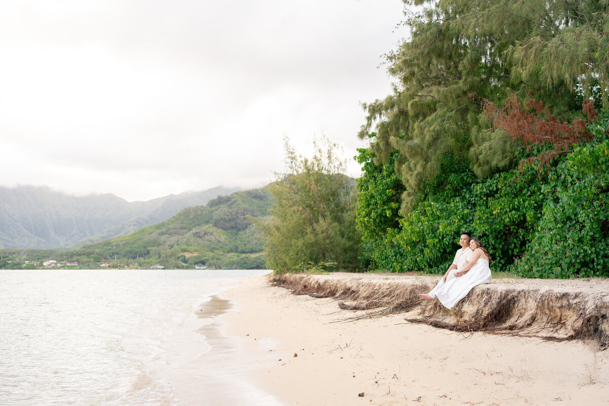 Oahu Hawaii Elopement Asian couple at Secret Island Beach during sunset with ocean waves and mountains.