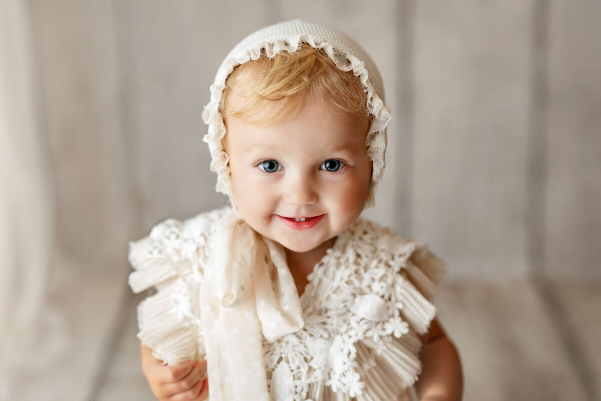 toddler with a bonnet and matching outfit smiling during a milestone photography session