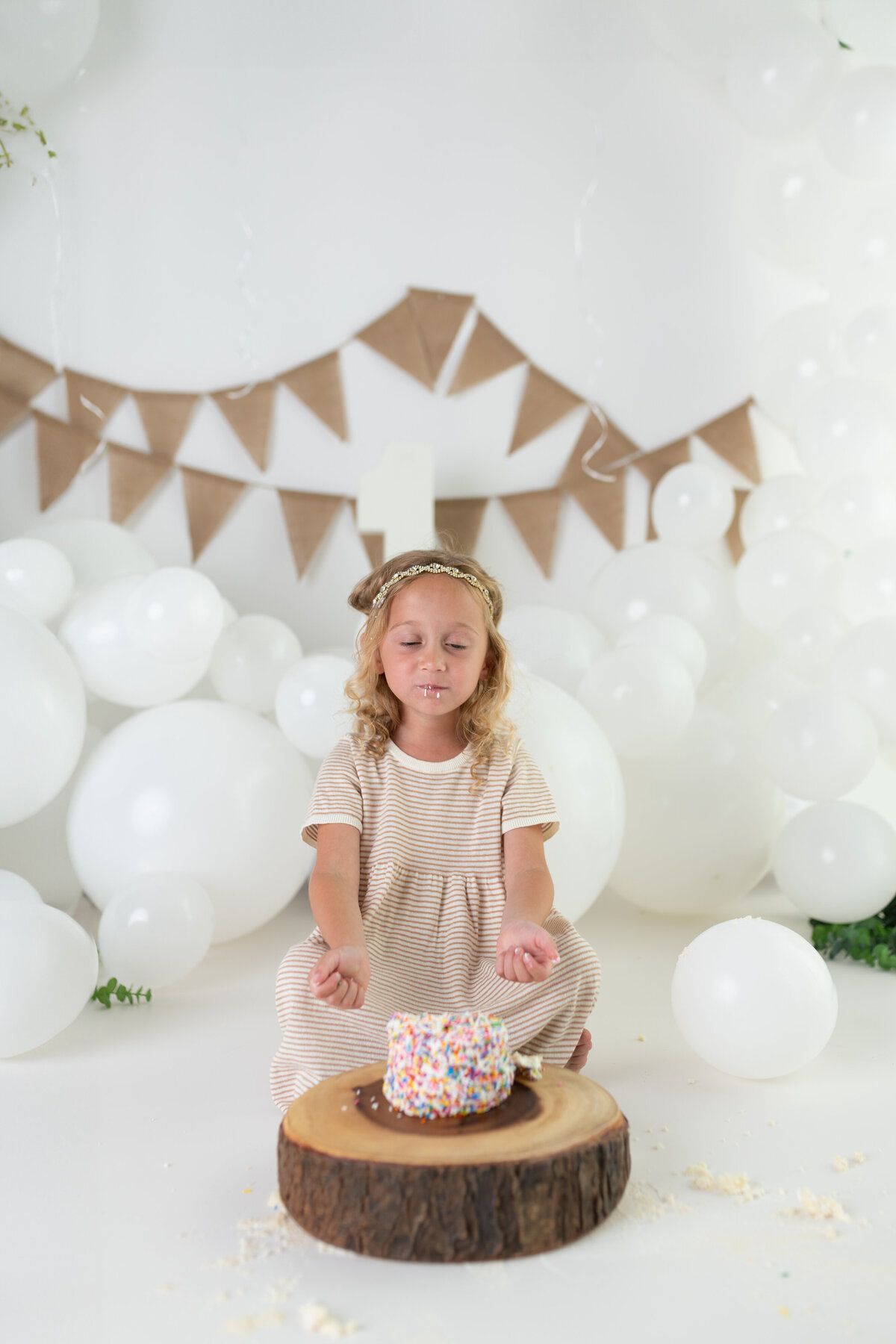 Cake smash milestone portrait of a five-year-old with a sprinkle-covered cake and a serene pose before the fun begins.