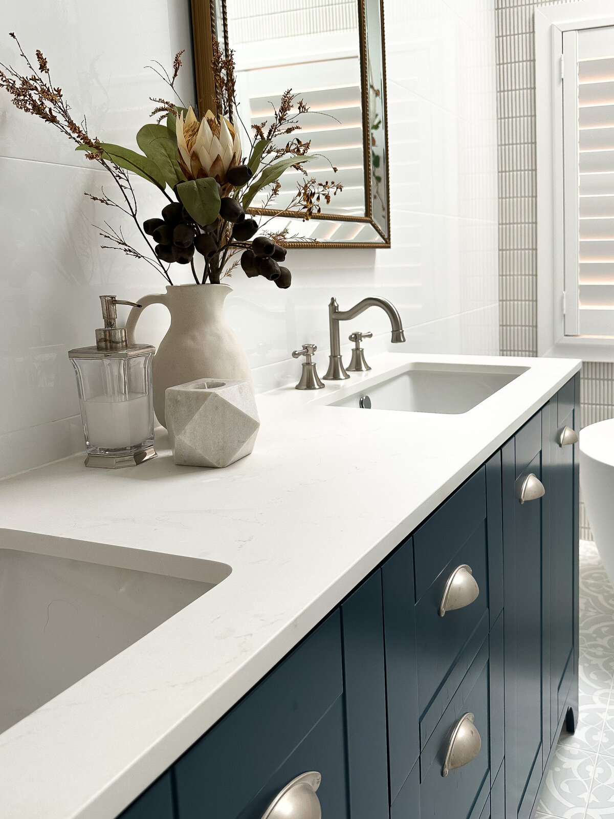 Bathroom designed by a Newcastle Interior Designer, featuring blue cabinets, a white countertop, dual sinks, and a vase with flowers.