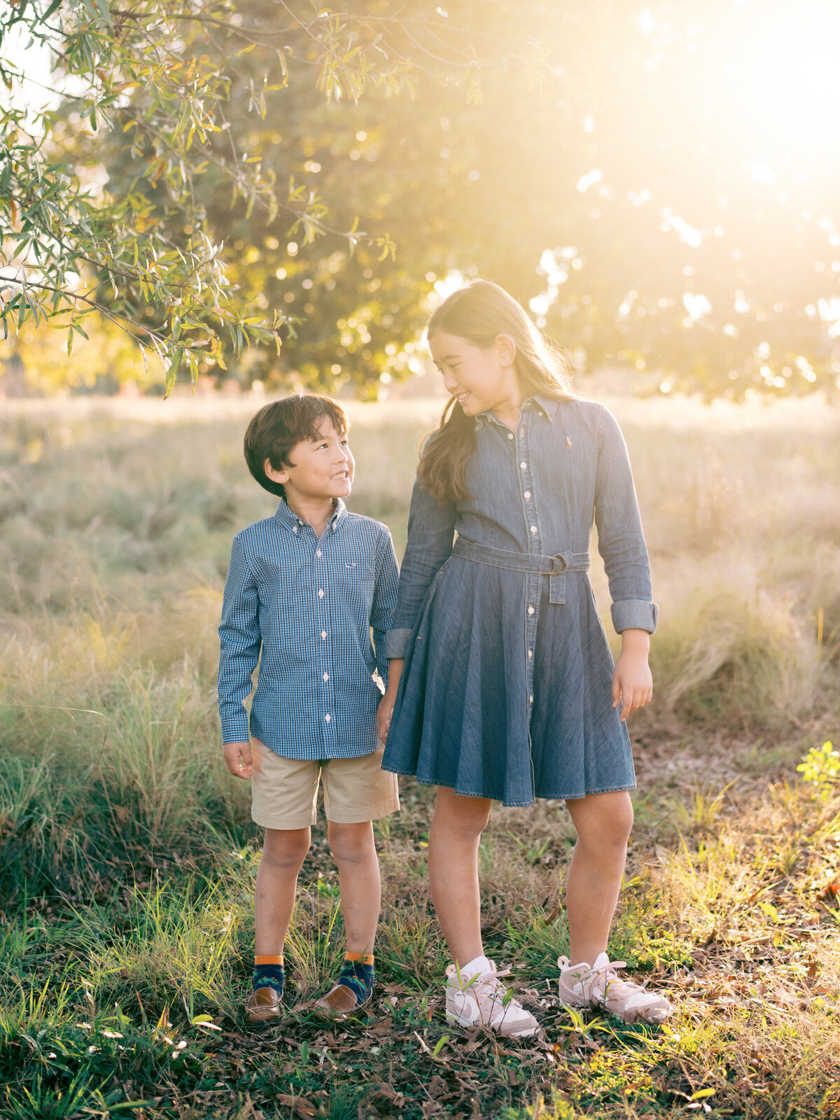 Siblings pose and smile at each other while backlit during this family session in Raleigh. Image by Raleigh maternity photographer A.J. Dunlap Photography.