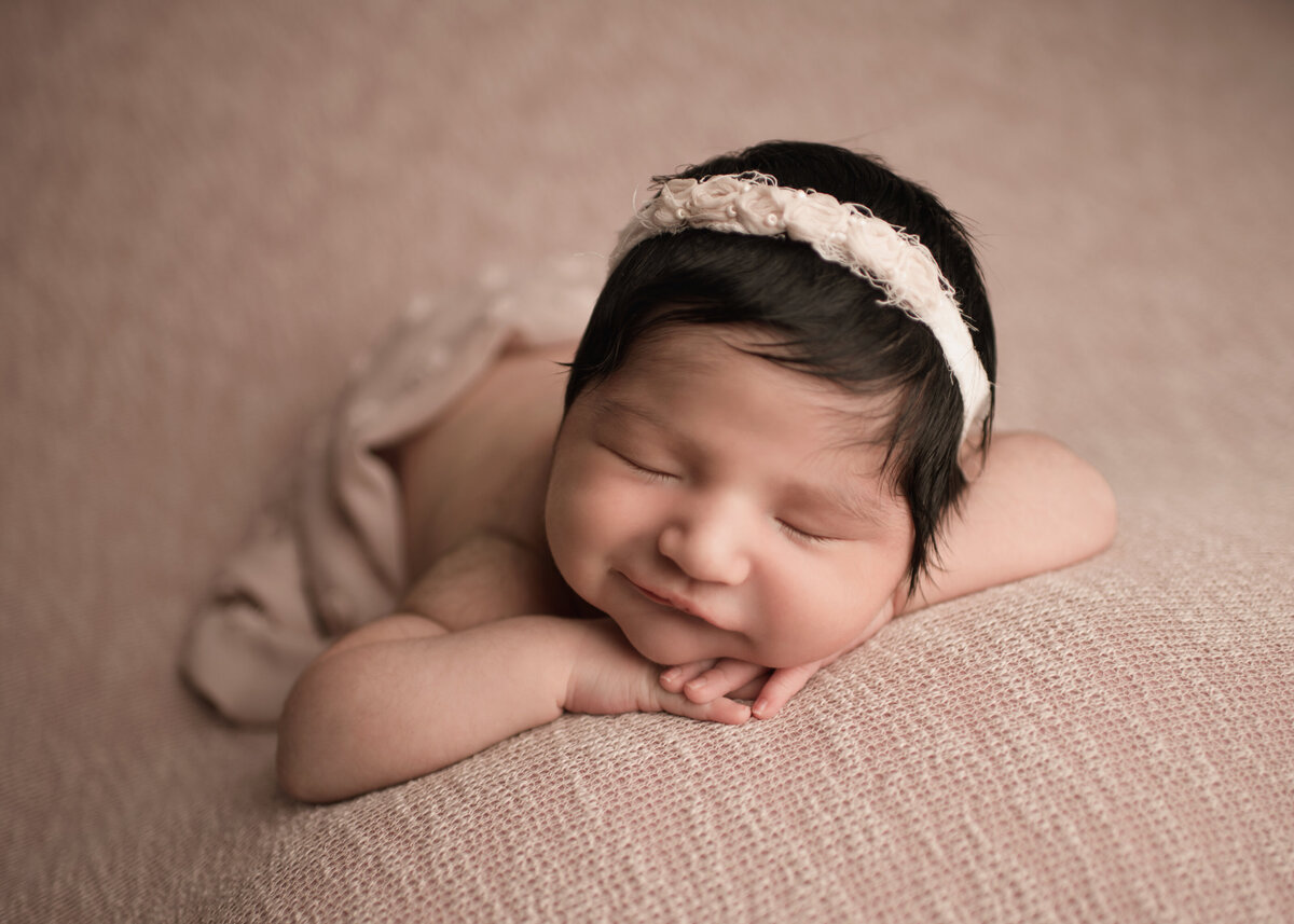 Aerial image of Riverside, CA newborn photoshoot. Baby girl sleeping on her belly and wearing a pale blush headband. Pale blush fabric is draped across her back. Her hands are folded under her chin. She is sleeping with a tiny smile.  Captured by Best Riverside, CA newborn photographer Bonny Lynn Photography.