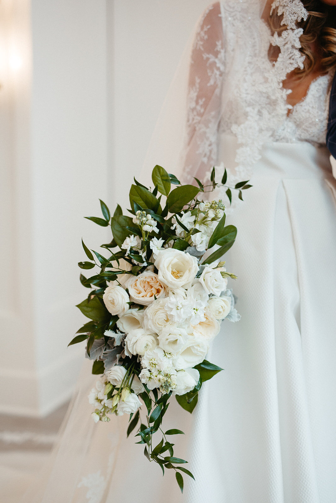 Close up of a white bouquet with greenery and a bride in a white wedding gown.