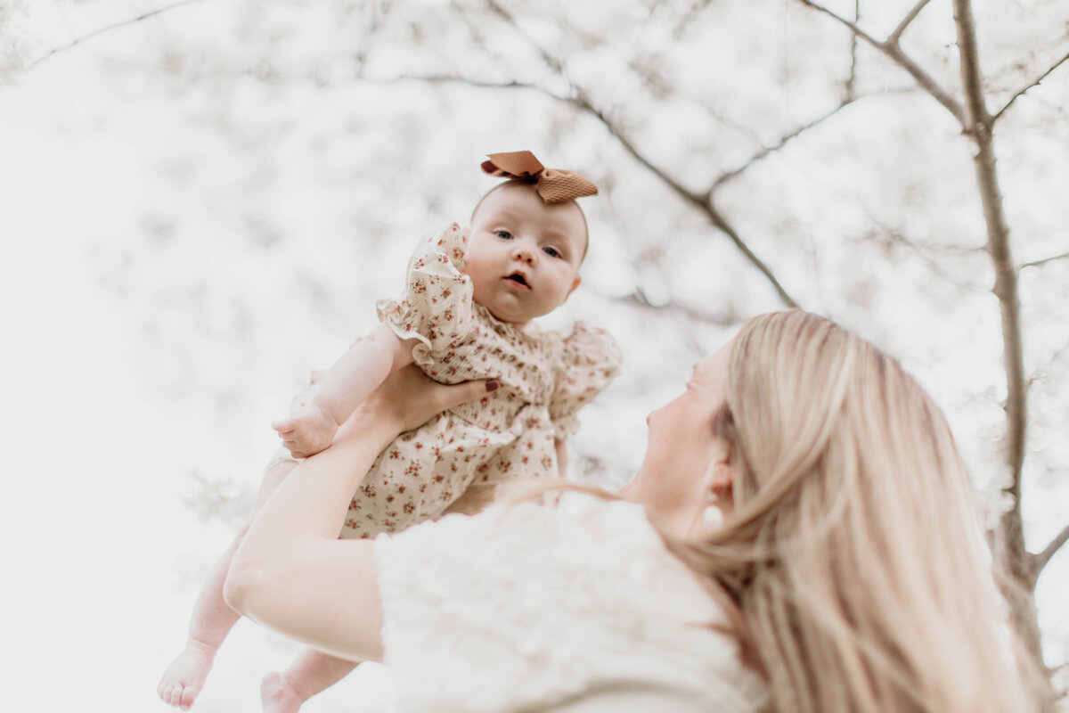 Mom holding baby in air with trees behind them. 