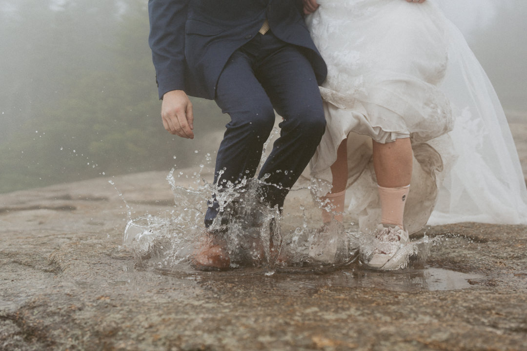 Bride and groom splashing in a mountaintop puddle in full wedding attire during their elopement on Mount Osceola.