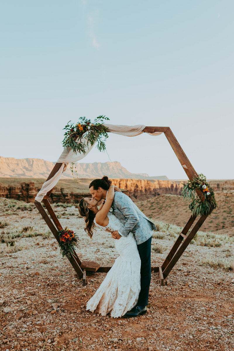 man and woman kiss in fron of arch with desert landscape behind them