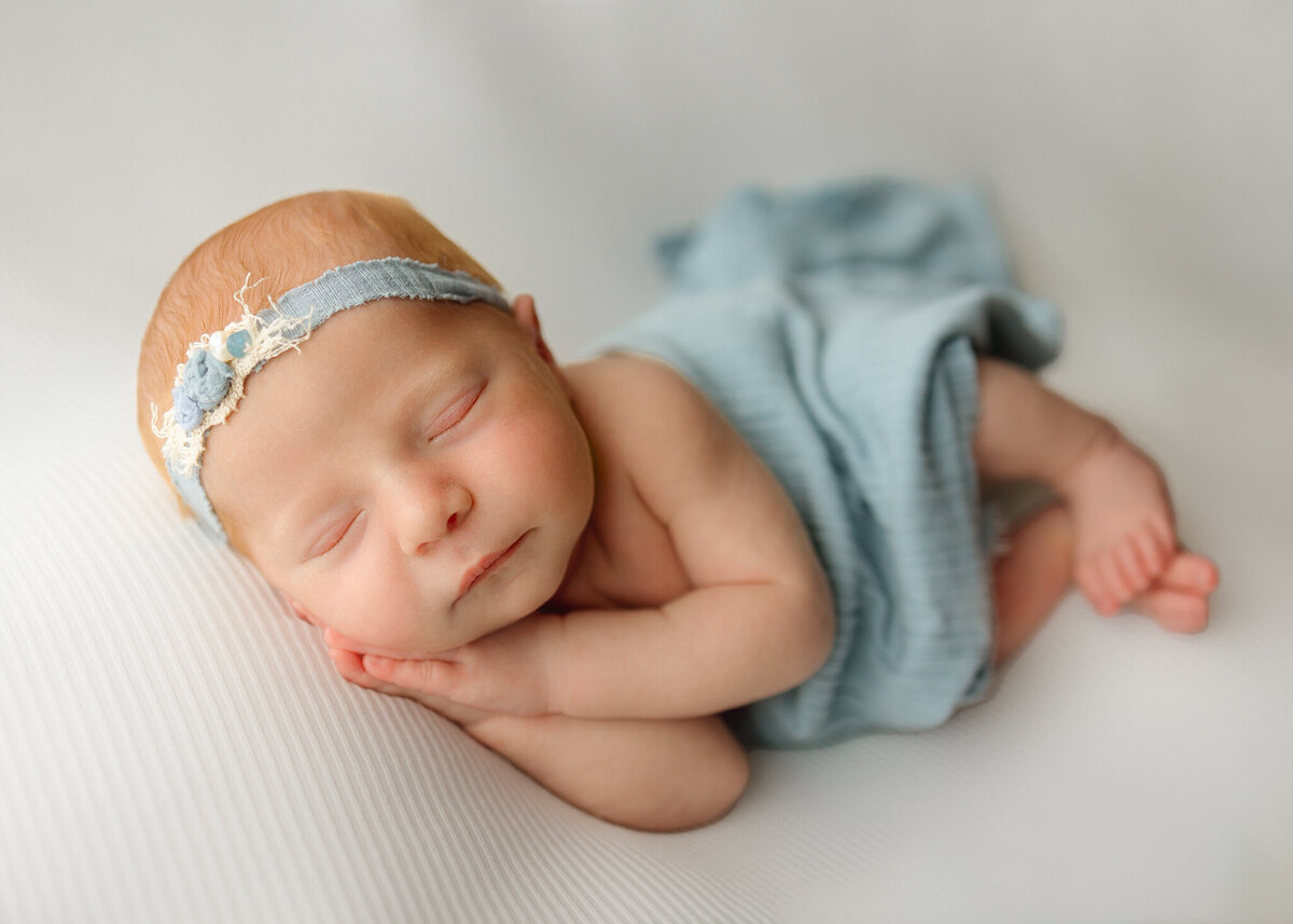 Baby girl wearing light blue fabric posing with hands together under her cheek