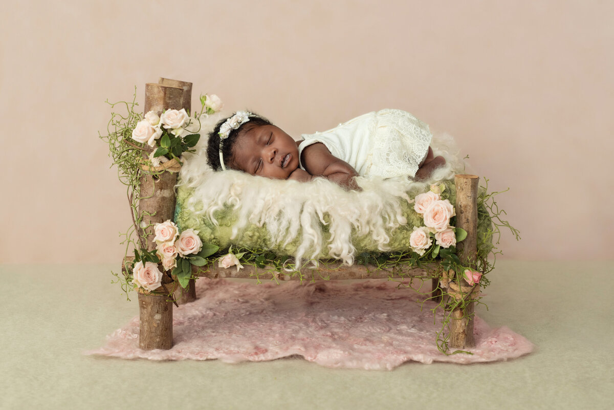 A newborn baby girl sleeps on a wooden bed in a studio in a white dress