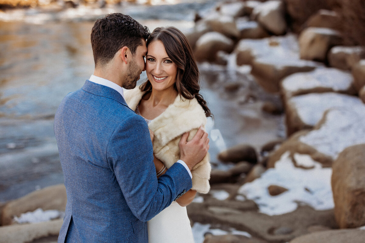 Groom kissing bride's cheek while standing near frozen river