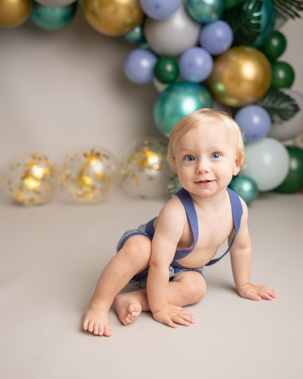 baby boy smiling in front of balloon garland for first birthday