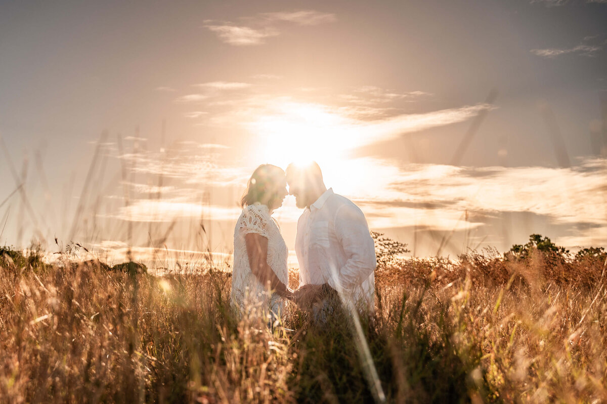 Silhouetted against a stunning sunset, a couple embraces in a serene field, symbolizing love and connection. - photo by Jamie Simmons