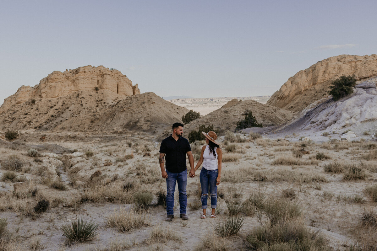 engaged couple standing together holding hands looking at each other in the desert