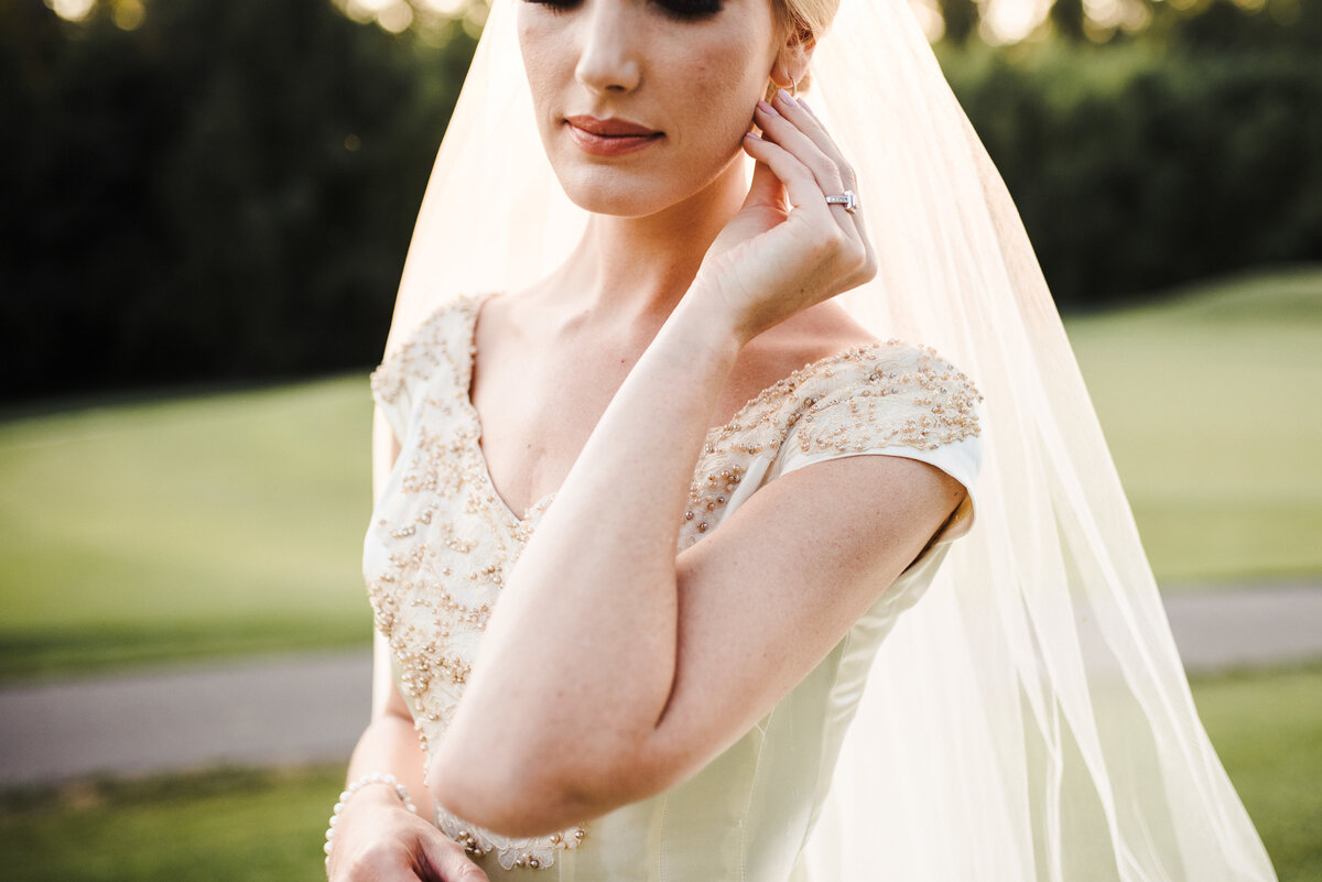 Half-body shot of the bride, holding her earring, with her wedding ring in her finger. Image by Jenny Fu Studio