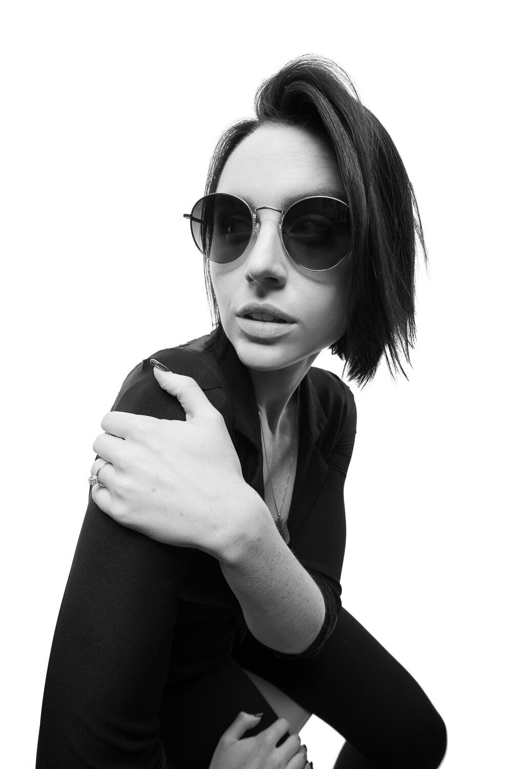 Fashion-forward personal brand photo of a woman leaning into the camera wearing sunglasses and a chic black outfit.