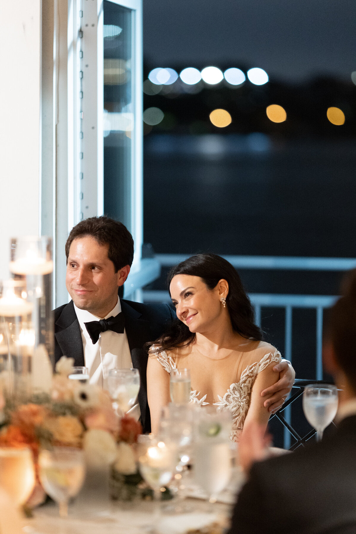 sarah smiles gently while her father gives a toast at their wedding reception