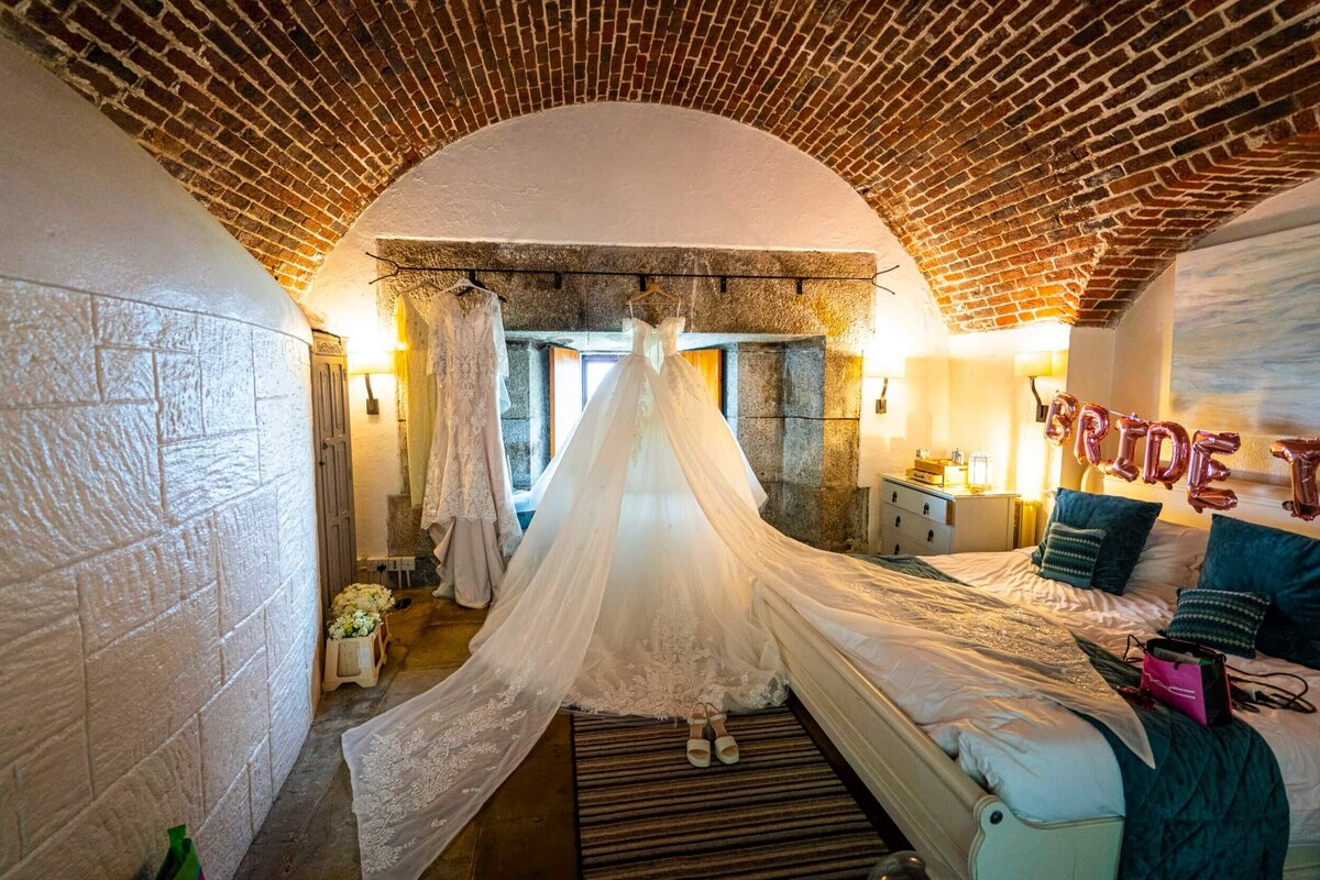 A room with a bed and a white wedding ress hanging in the window