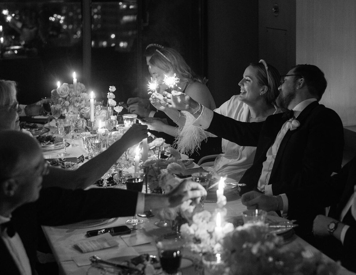 Couple in black and white lighting a sparkler at their intimate wedding reception