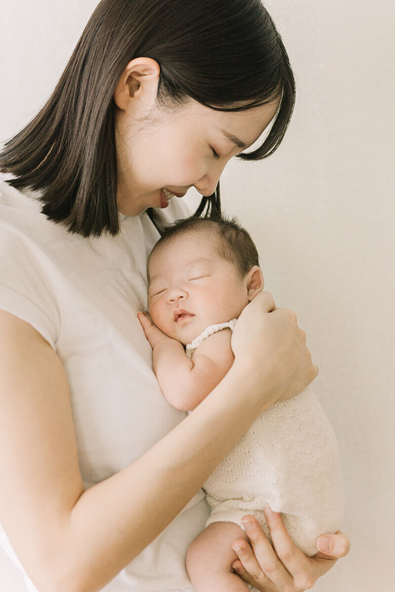 赤ちゃんに顔を寄せて笑っているママが美しい、シンプルでオシャレな白を基調としたニューボーンフォト