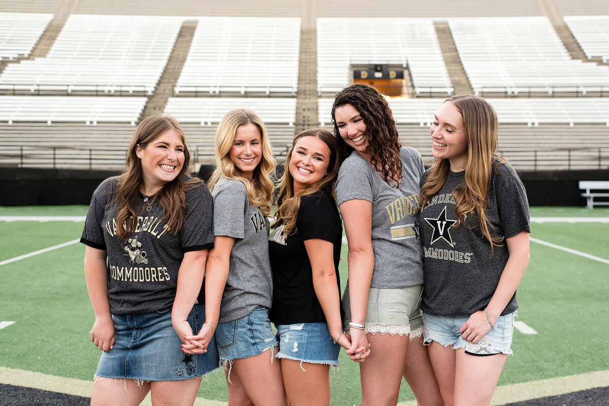 5 Senior Girls holding hands and laughing together standing on the college football field at Vanderbilt University