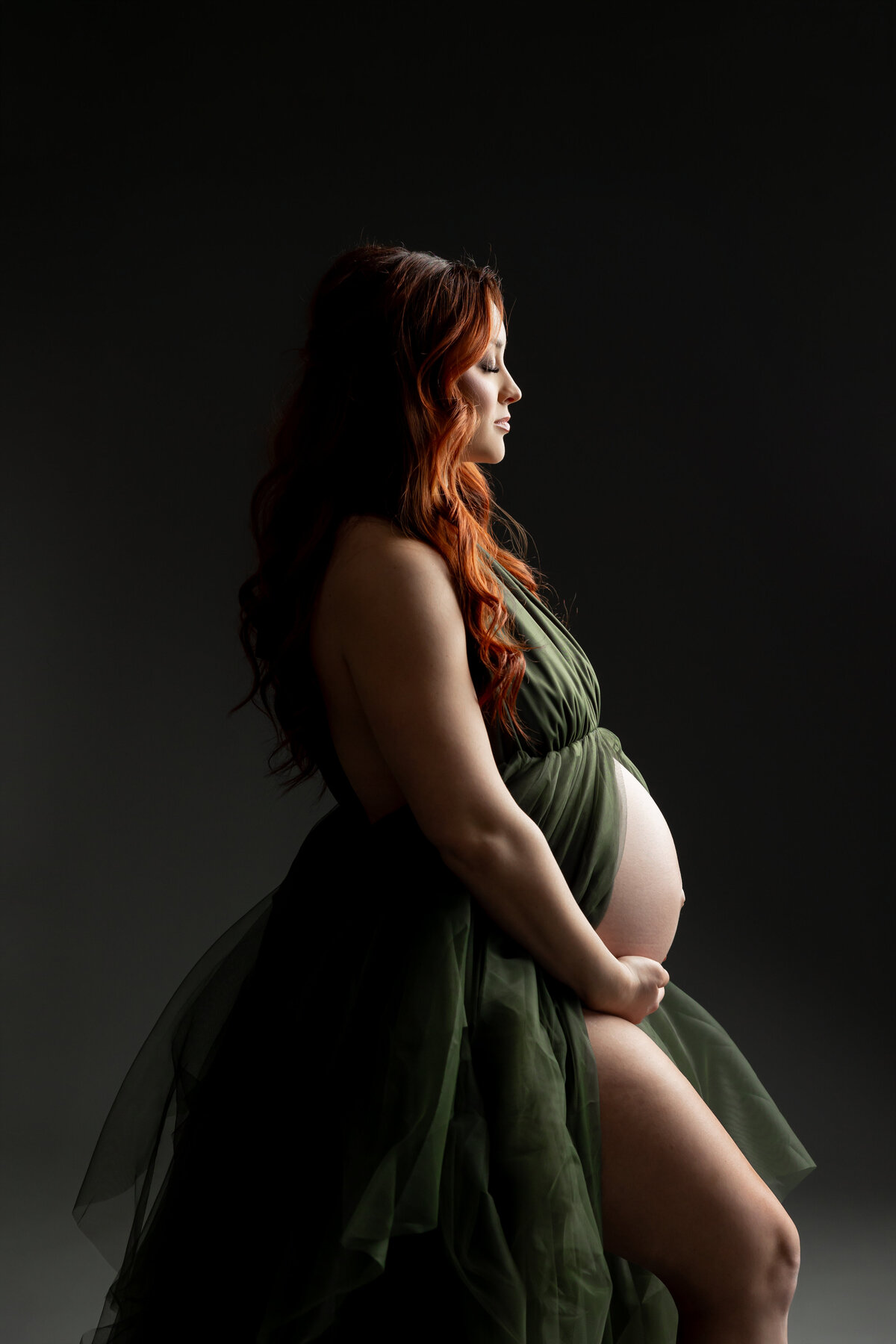 In a black dress, she poses in a side view, her silhouette highlighted by soft lighting, exuding elegance and calm. Captured by Inland Empire photographer Kaitlyn Dawn Photography.