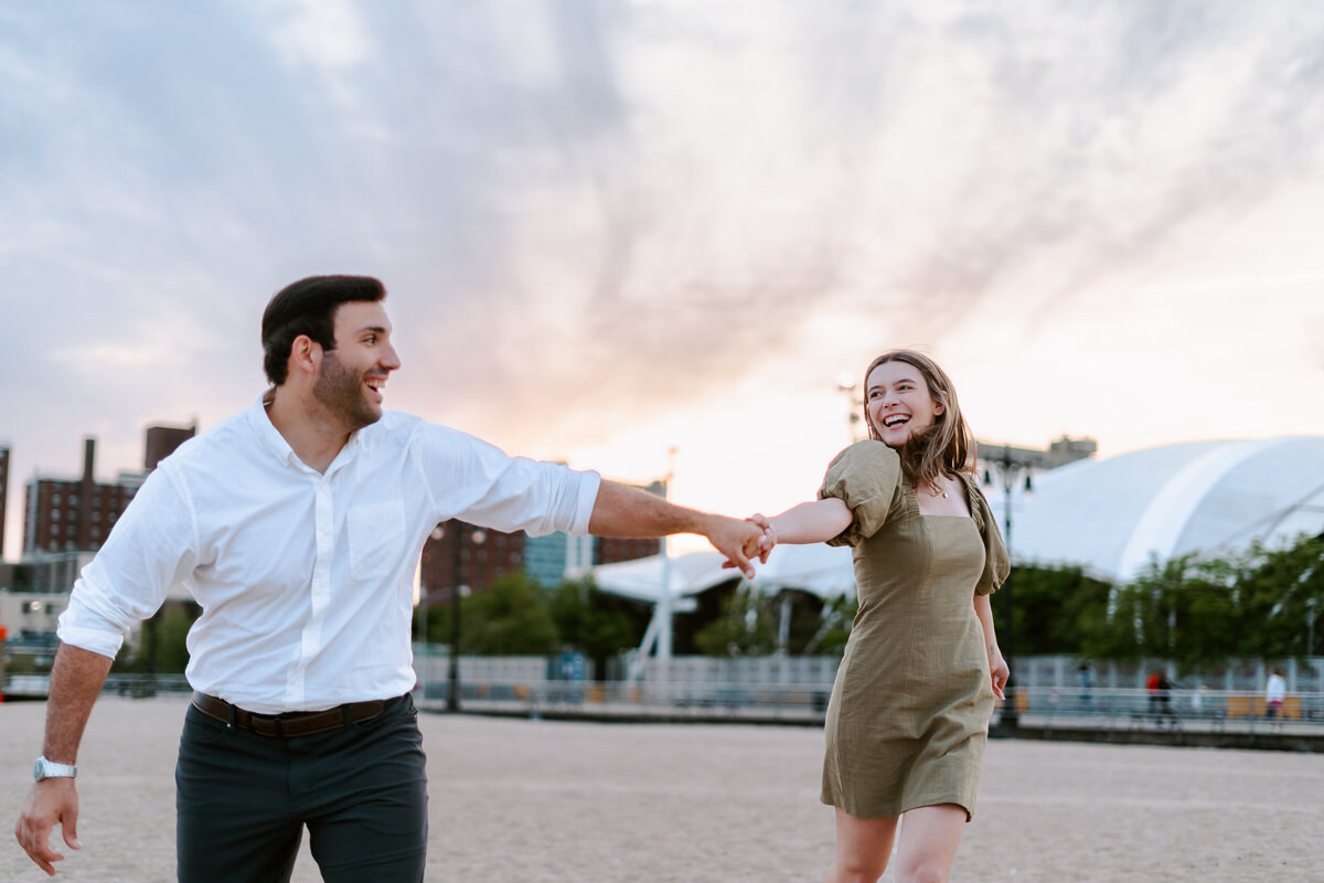 Couple skipping on the beach hand in hand during their spring engagement photo session at Coney Island Beach