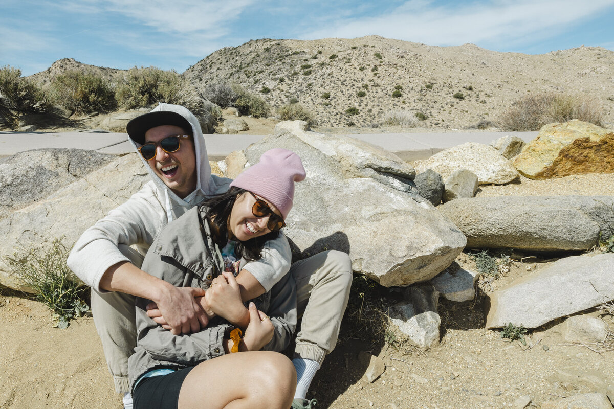 A couple holds one another leaning against rocks.