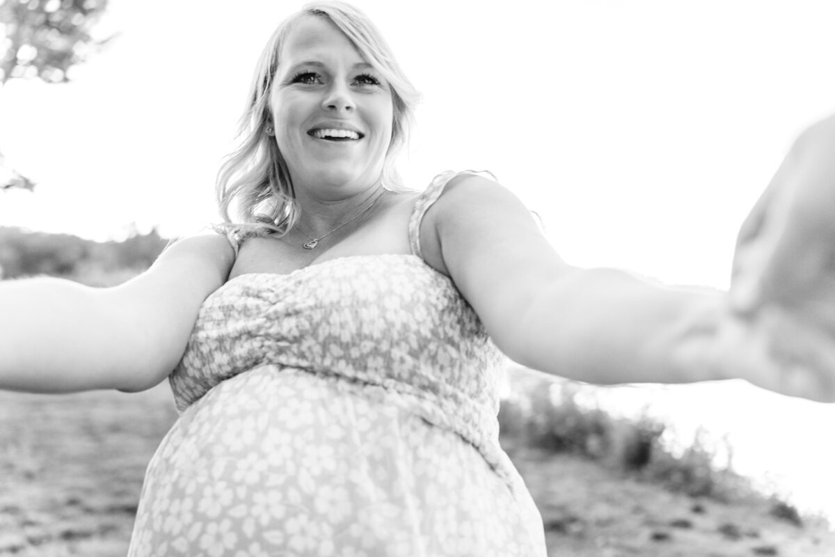 A close-up, black and white shot of the pregnant woman smiling and extending her arms, as if reaching out to someone.