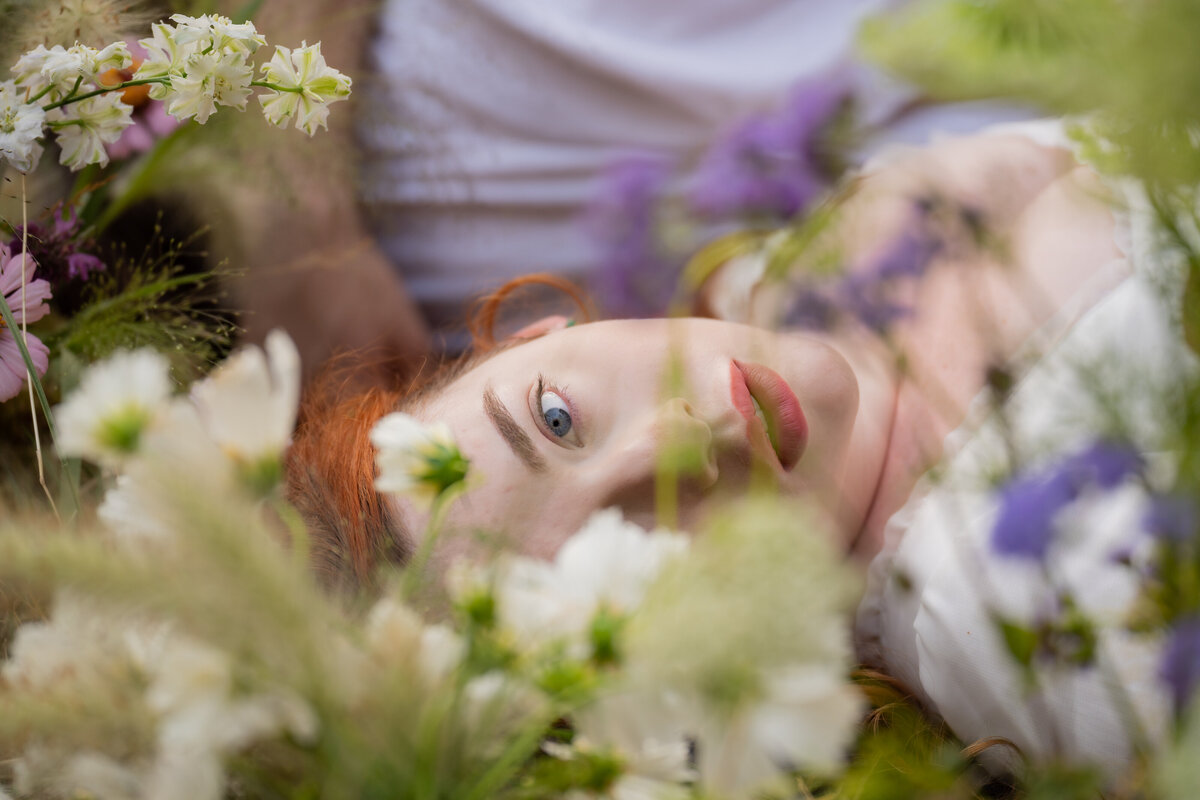 A person laying in the grass with flowers in front of their face
