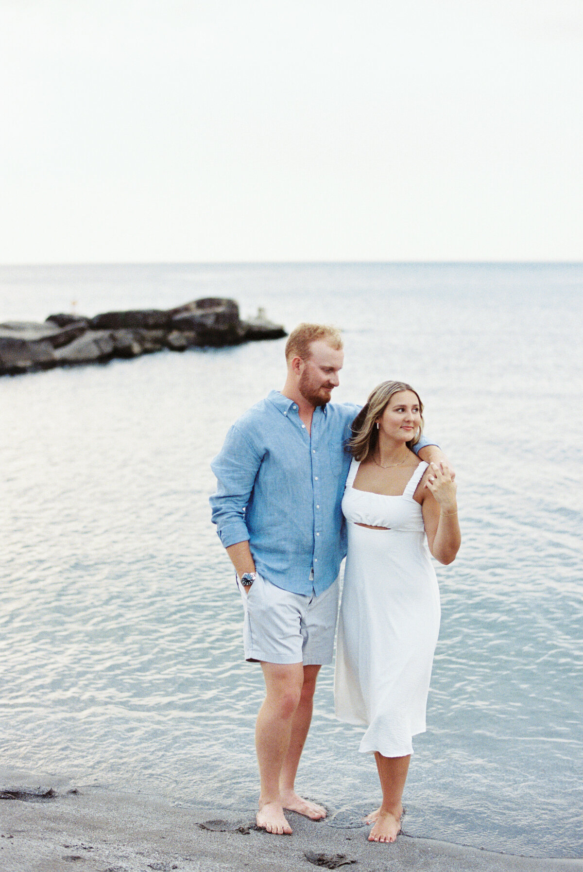 Engaged couple standing by Lake Erie waterline at Edgewater Beach during their engagement session.

