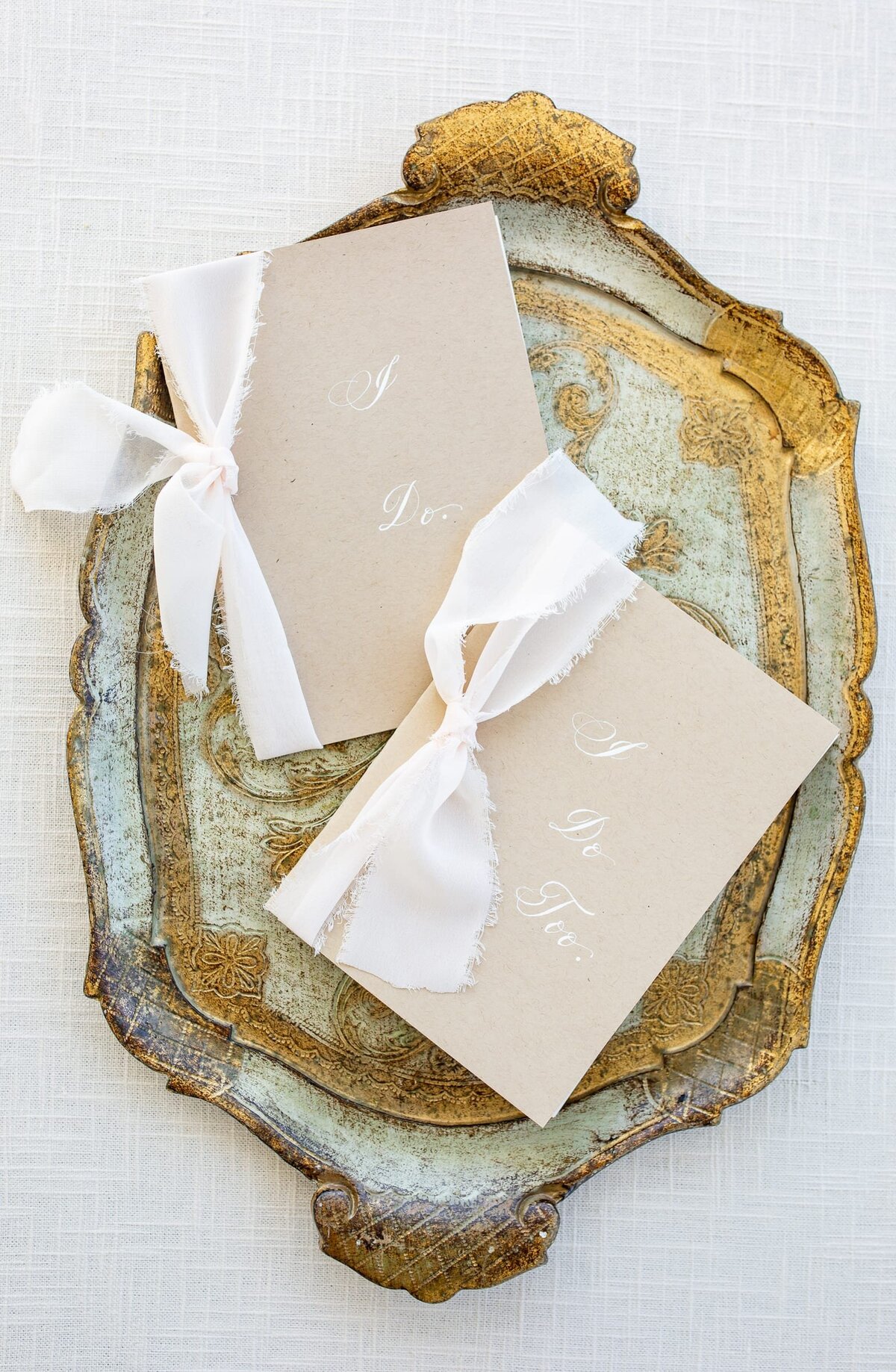 Wedding vow booklets with white ribbons and words:" I Do" and "I do too" on a vintage tray. 